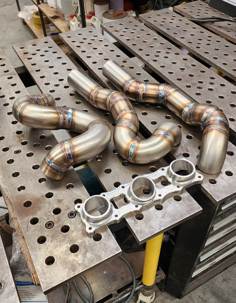 CNC machined flange with three exhaust runners tacked in place before final welding, showing initial manifold assembly alignment